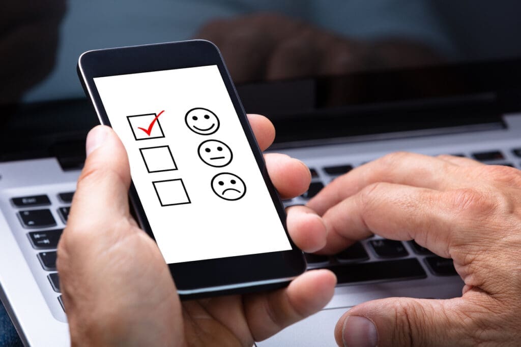 CAN-SPAM Compliance Checklist: Close-up Of A Man's Hand Holding Smartphone With Ticked Checkbox And Smile Icon On Screen