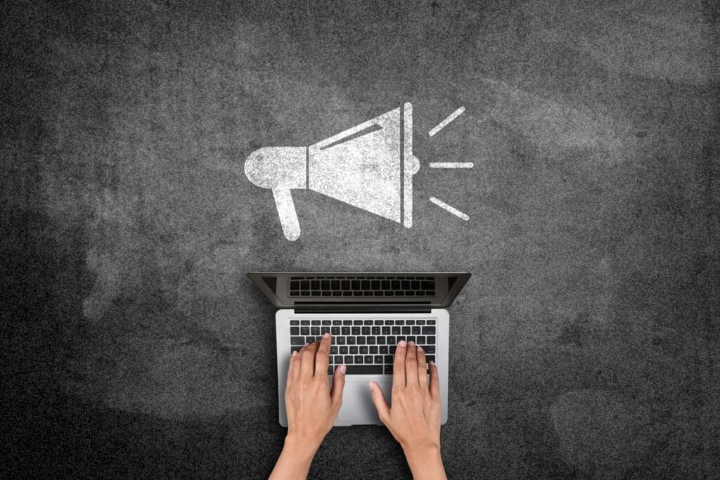 Online Marketing Strategies for Recruitment - Job Boards: Aerial view of hands typing on laptop with megaphone icon above