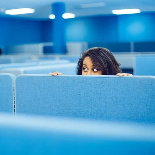 Not Setting Goals - Dark-haired woman peeking over cubicle wall